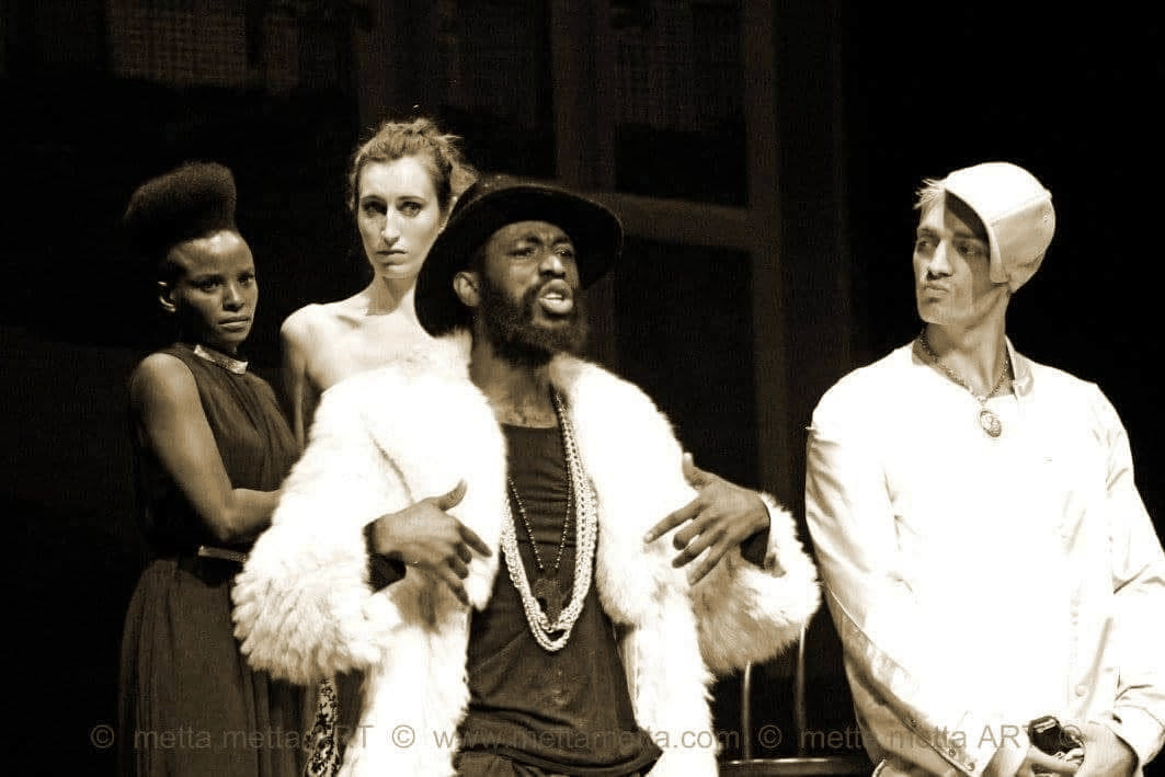 Sepia ensemble still from The Merchant of Venice showing Portia, Nerissa, the Prince of Morocco, and another suitor on stage.